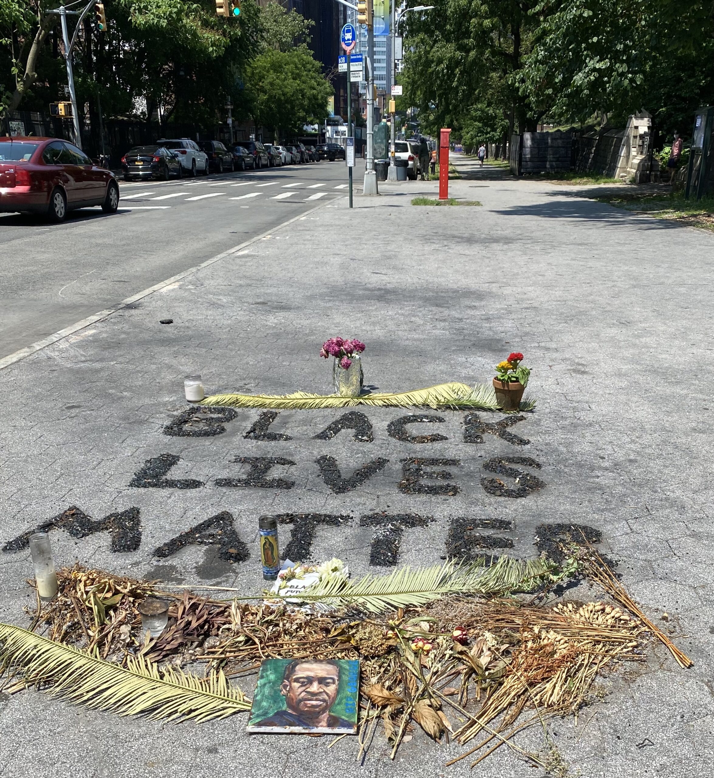 Image of Black Lives Matter written on the ground with dry flowers and a picture of George Floyd.