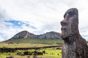 Image of a moai statue and a cliff in the distance. 