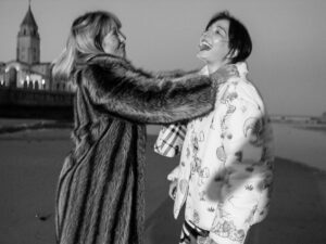 Image of a film still from El Planeta: black and white photo of one a woman choking another woman while wearing winter coats.