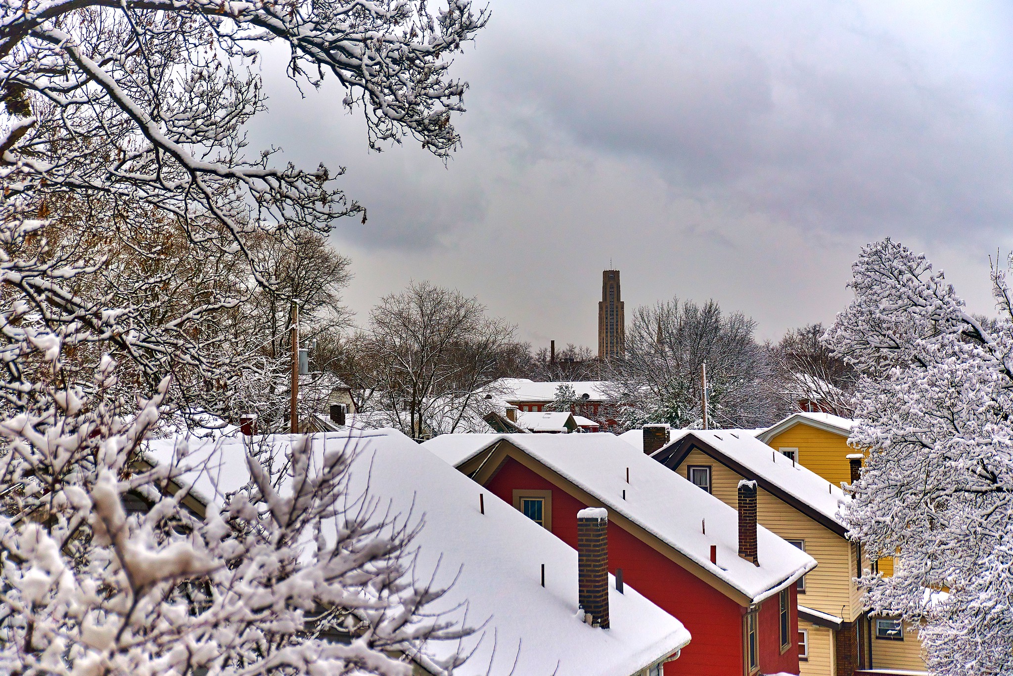 Snow lying on rooftops and trees with a background of a cloudy sky.