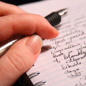 Image of a hand holding a black pen over a spiral notebook with some writing.