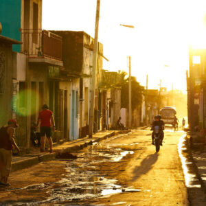 Image of a street with puddles, two-story houses, and a biker, sepia toned.