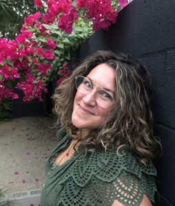 Headshot of Xochitl Gonzalez, wearing a green blouse with a bright pink bush in the background.