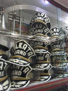 Images of marching band hats stacked in a glass case, with "Kolkata Band" written across each one.