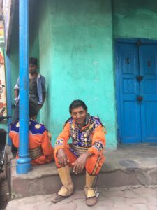 Image of a marching band member sitting on a stoop, dressed in orange with blue highlights.