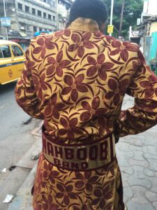 Image of a back of a marching band member with "mahboob" written across his waist, dressed in orange and red.