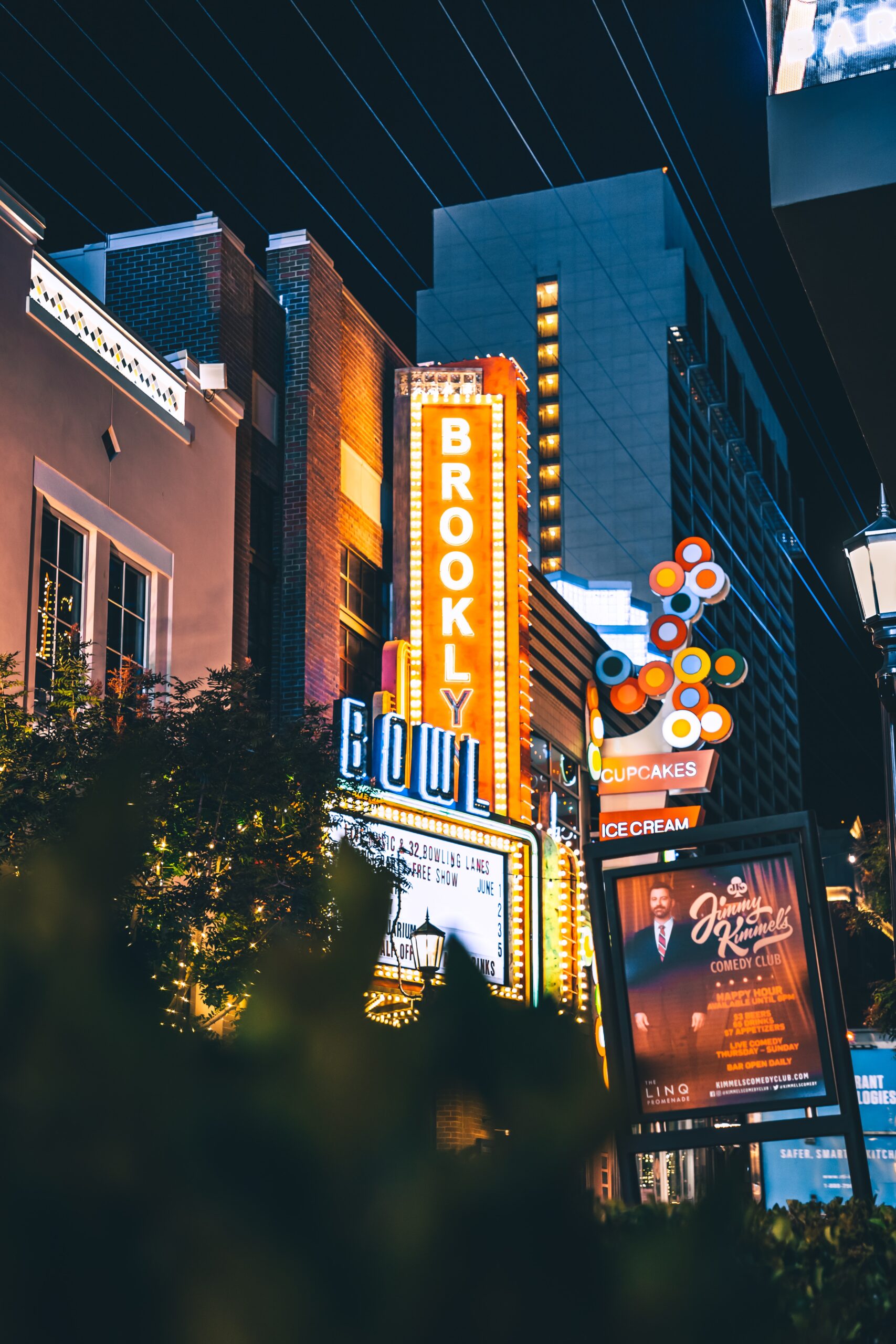Signage in New York City at night. A lit vertical sign reads BROOKLYN, above a movie theater sign and a colorful sign for an ice cream parlor.
