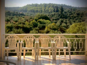 Image of a row of chairs on a balcony with tree tops in the background.