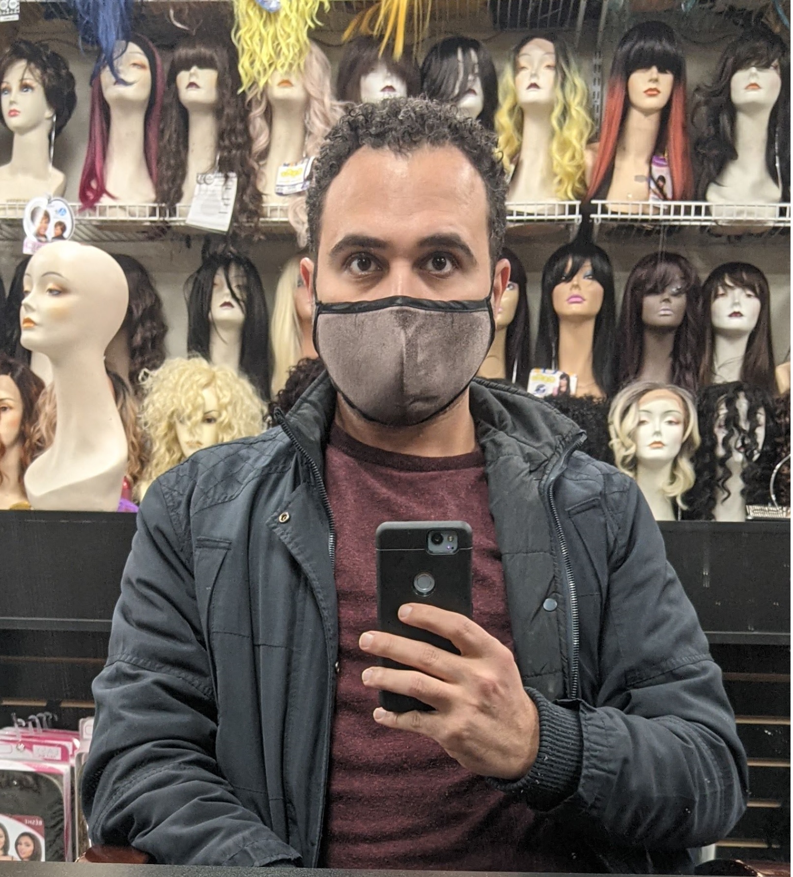 Image of Ahmed Naji in front of a wall of wig mannequins, taken as a mirror selfie.