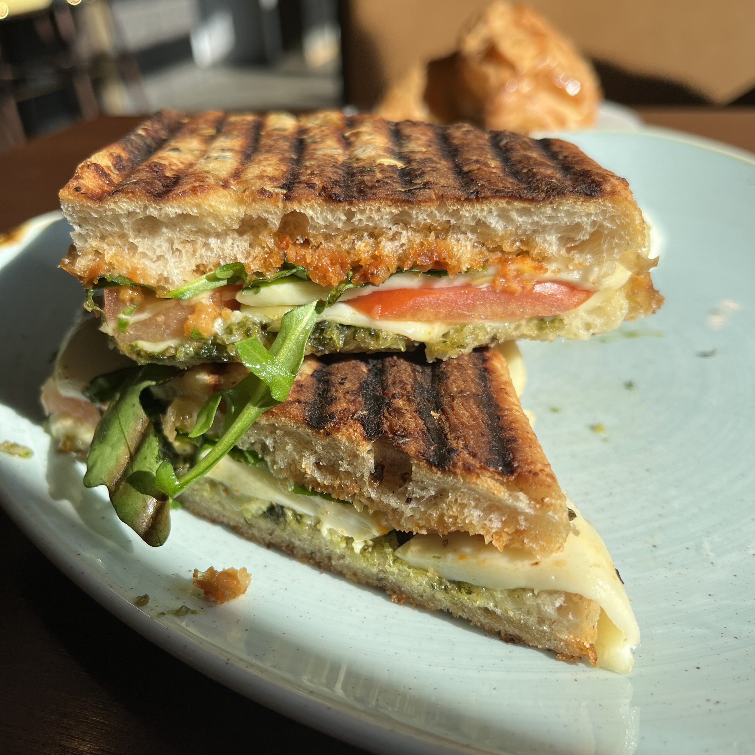 Image of a panini with tomato, cheese, and arugula, sliced in half.