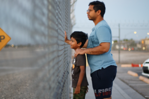 A man and a boy face a metal fence.