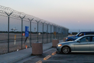 A row of cars parked in front of a metal fence.