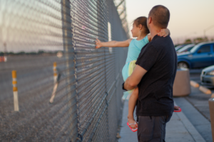 a man holding a child in front of a fence. the child is touching a fence.