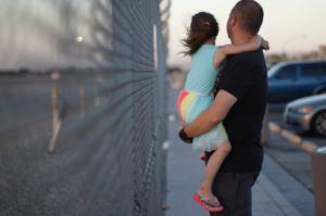 A man holding a girl in front of a metal fence.