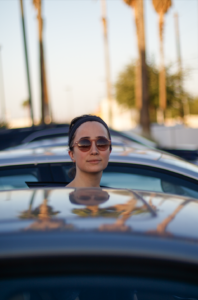 Woman behind a car with palm trees in the background.