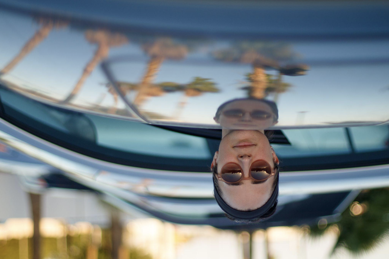Woman sticking her head from behind a car, upside down.