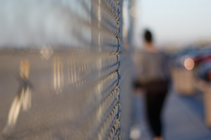 Blurry image of a woman standing against a fence.