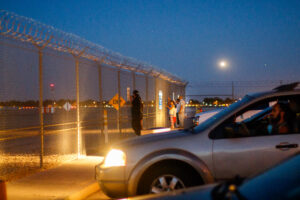 A person stands in front of a metal fence in the twilight.