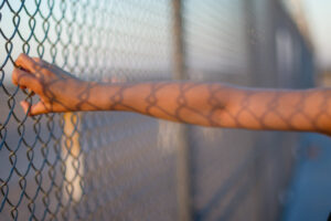 Hand holding onto a chainlink fence.