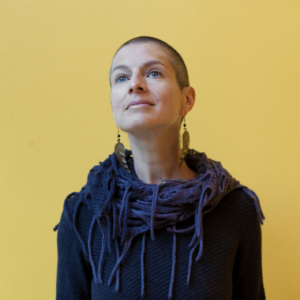 Anna Badkhen's headshot: woman in a navy sweater and purple scarf against a white background.