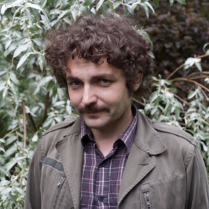 Boris Dralyuk's headshot: a man with curly brown hair against a tree.