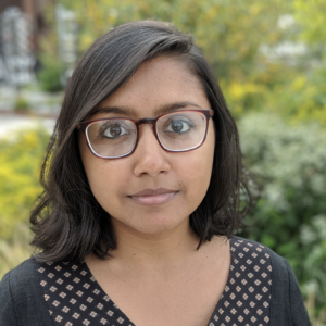 Megha Majumdar's headshot: a woman dressed in black against a background of greenery.