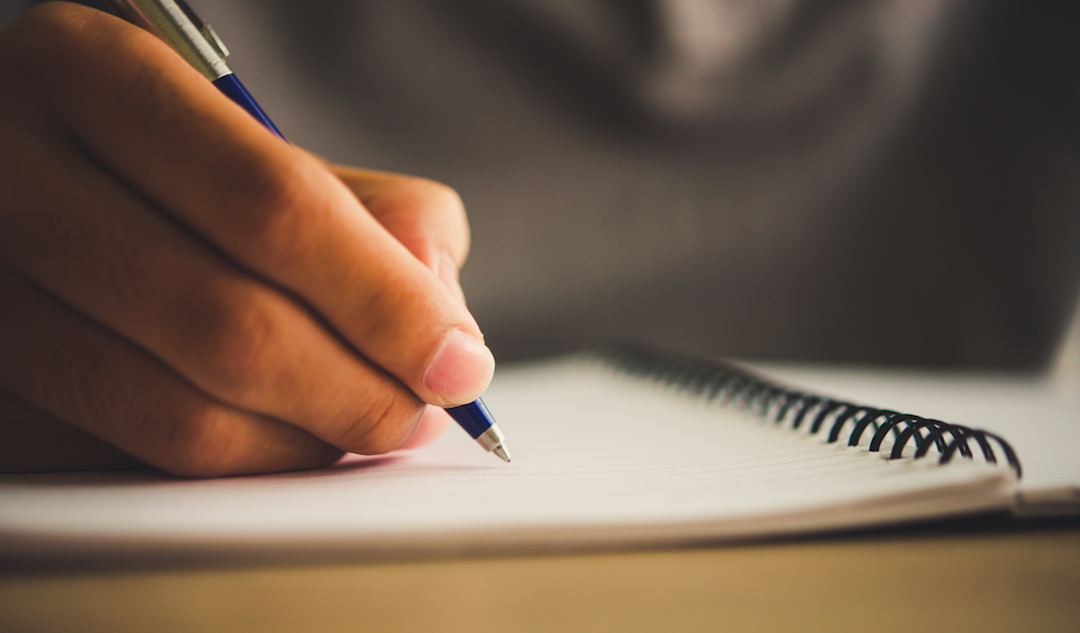 Hand holding a pen over a spiral-bound notebook.