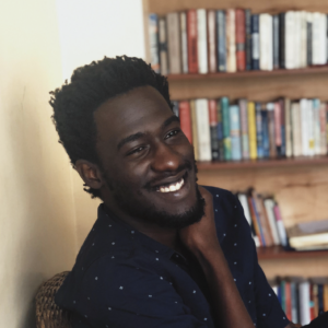 Carey Baraka's headshot: black man in a navy shirt with a bookcase in the background.