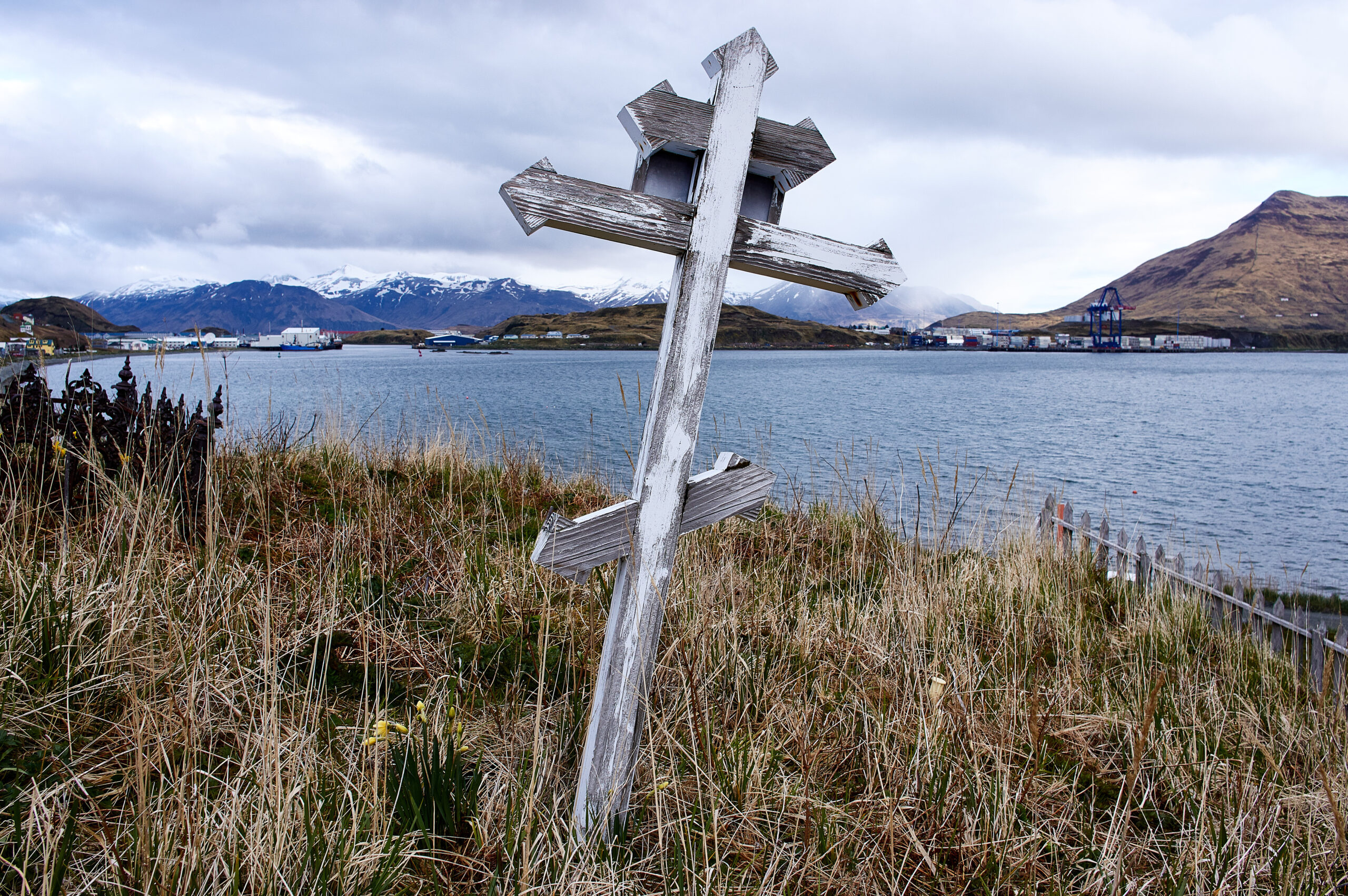white, wooden cross on the shore of a river. the colors of the image give off a pale-ish atmosphere, like a storm is coming