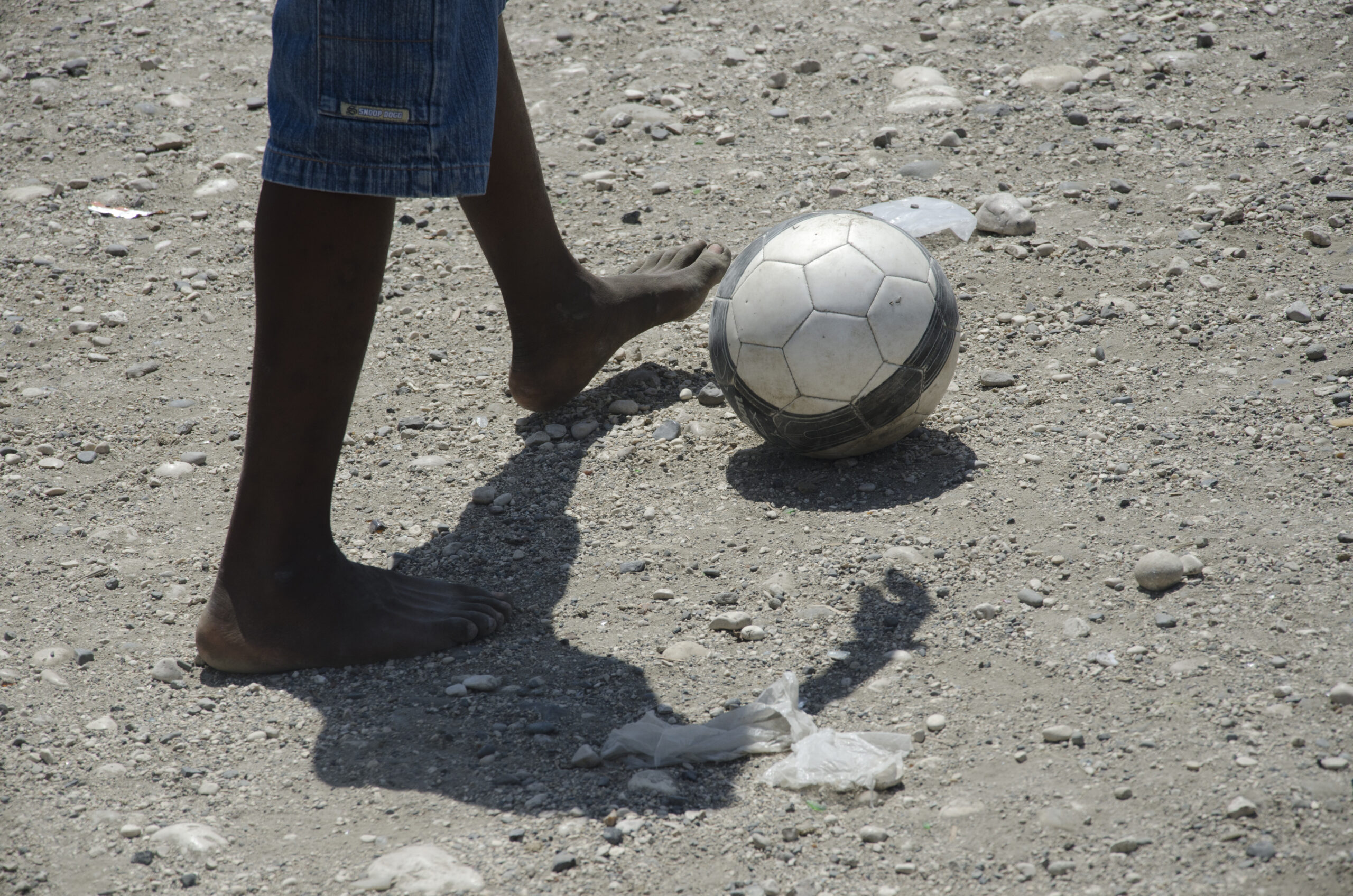 Image of bare feet kicking a soccer ball.