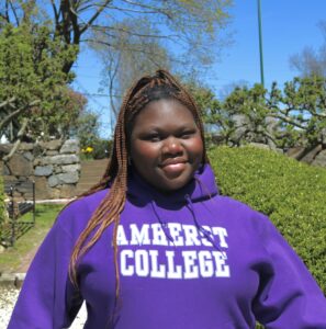 Headshot of Morry Ajao: Black woman in an Amherst College sweatshirt in front of greenery.