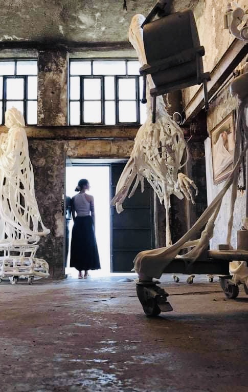 an image of a woman among old artifacts. the woman's back is to the photographer and she is facing the open door