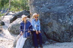 Two elderly women sitting on a boulder in a forest.
