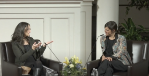 Jennifer Acker and Valeria Luiselli sitting on stage sitting in leather seats with a bouquet of flowers between them,