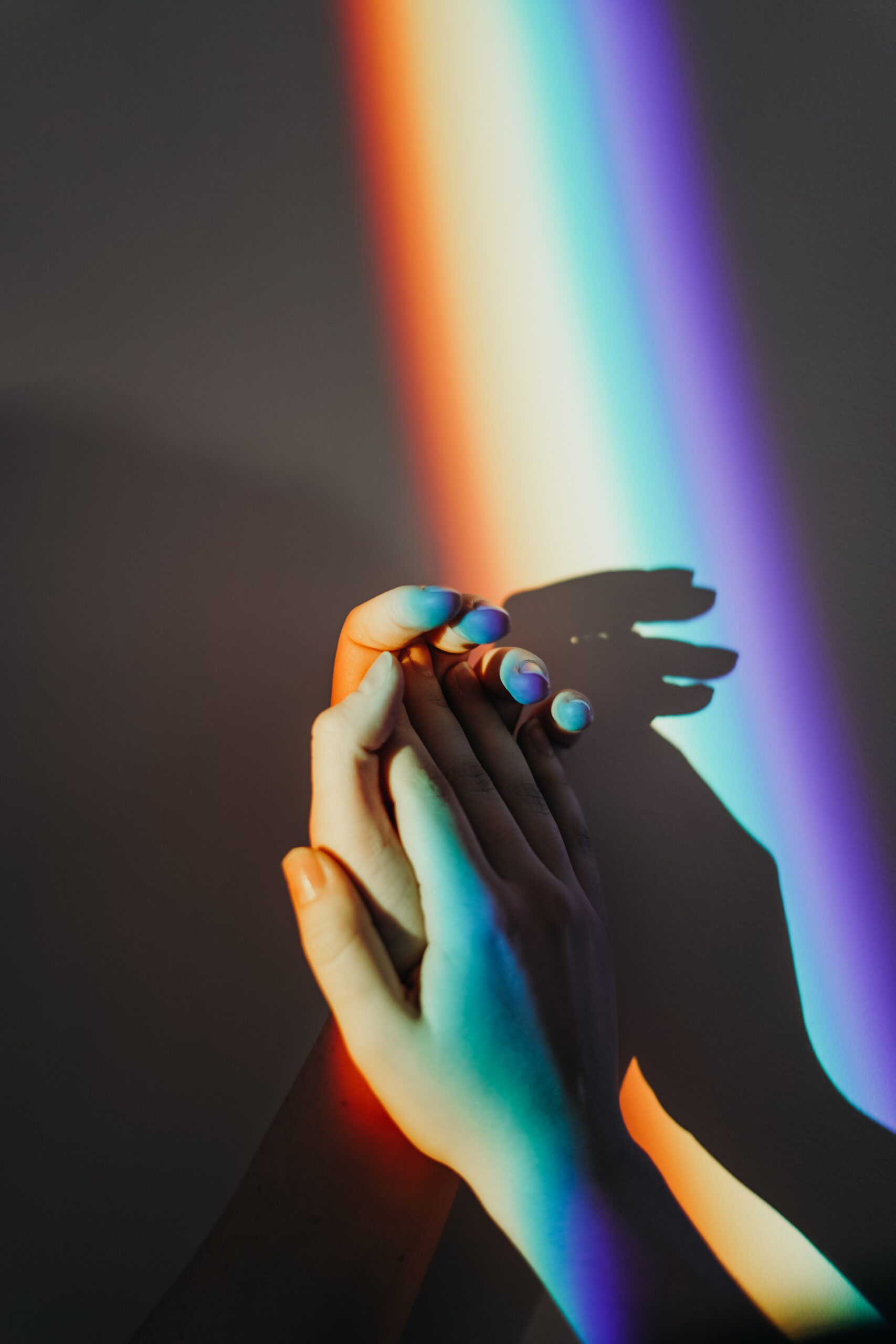 Two hands meet, palm-to-palm. Rainbow light cascades over the hands.
