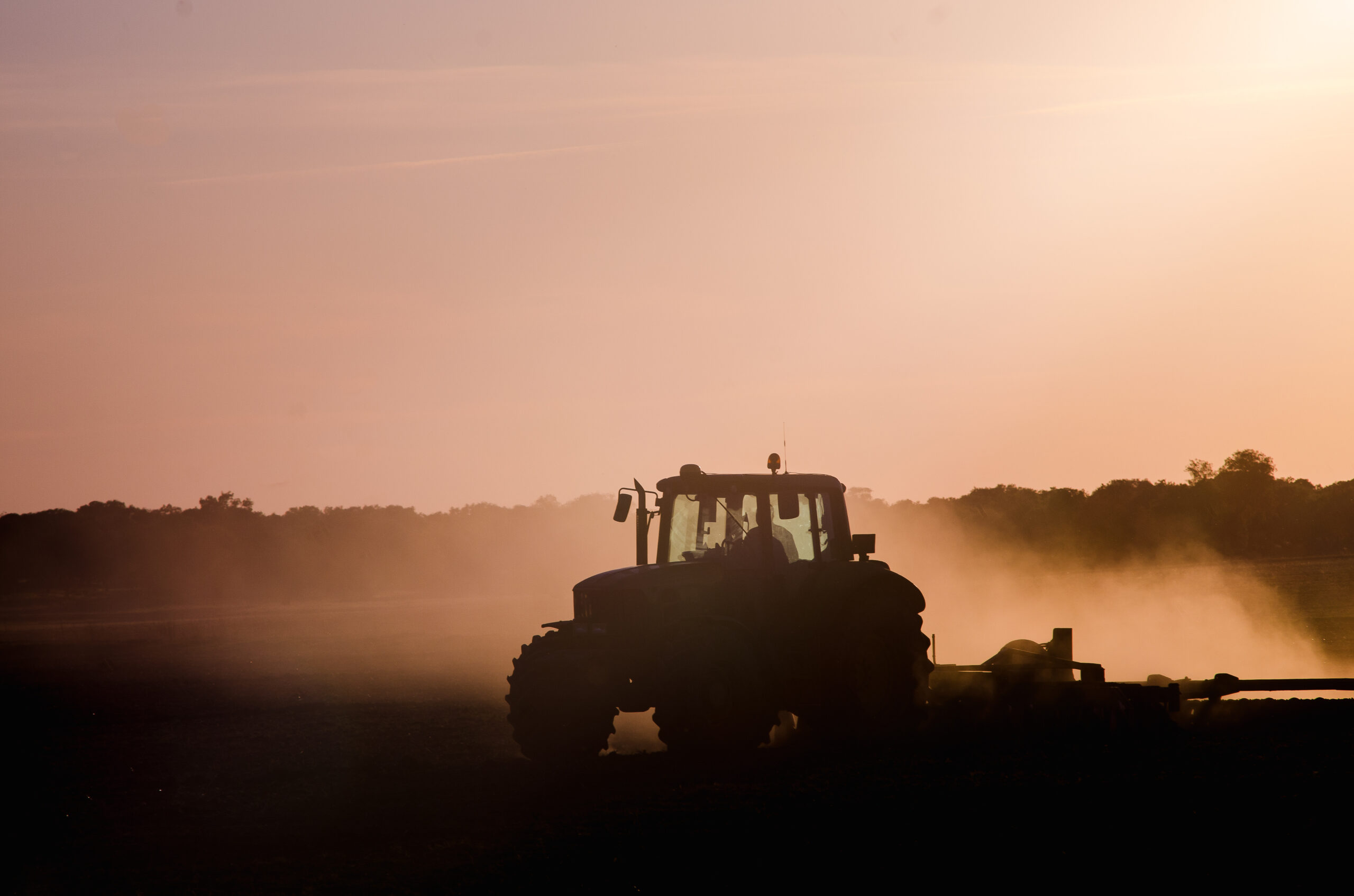 Silhouette of a tractor on a dusty field at sunrise