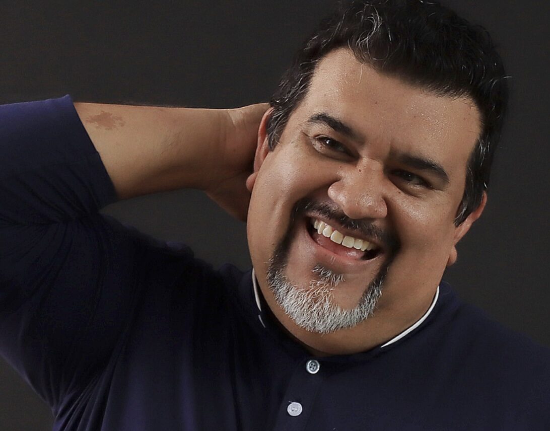 Portrait of Lupe Mendez smiling in a navy blue shirt, with his hand behind his neck.