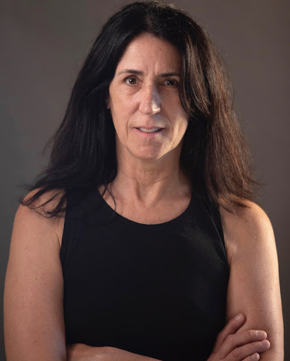 Jennifer Martelli's headshot: A woman with thick brown hair looks intently and inquisitively at the camera, arms crossed.