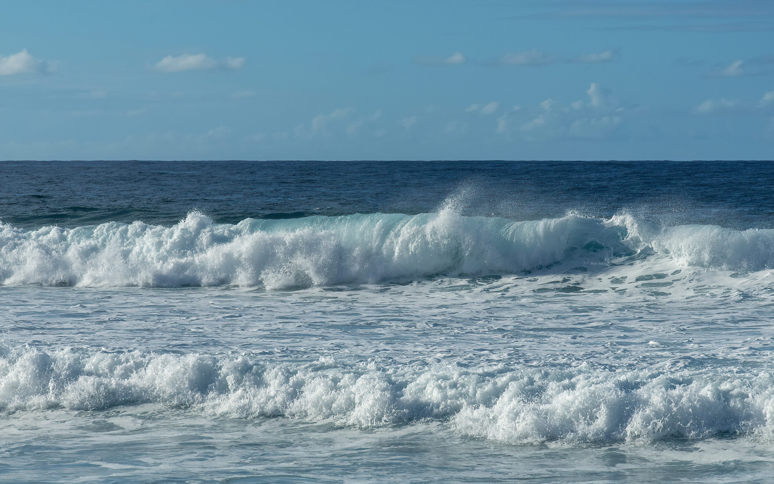 Ocean waves breaking on the shore. The sky and sea are bright blue.