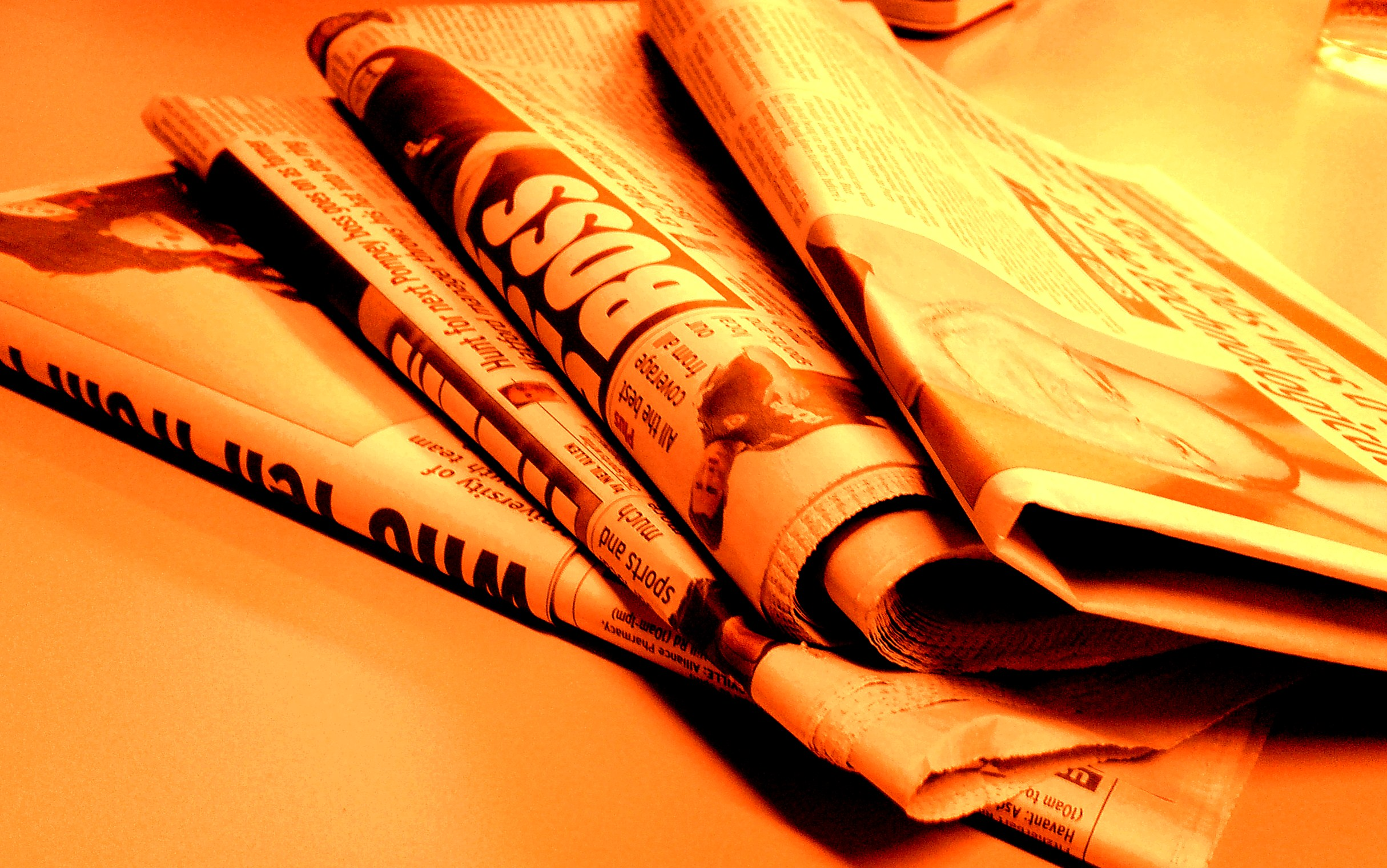 A stacks of newspapers, folded in half and bathed in orange light.