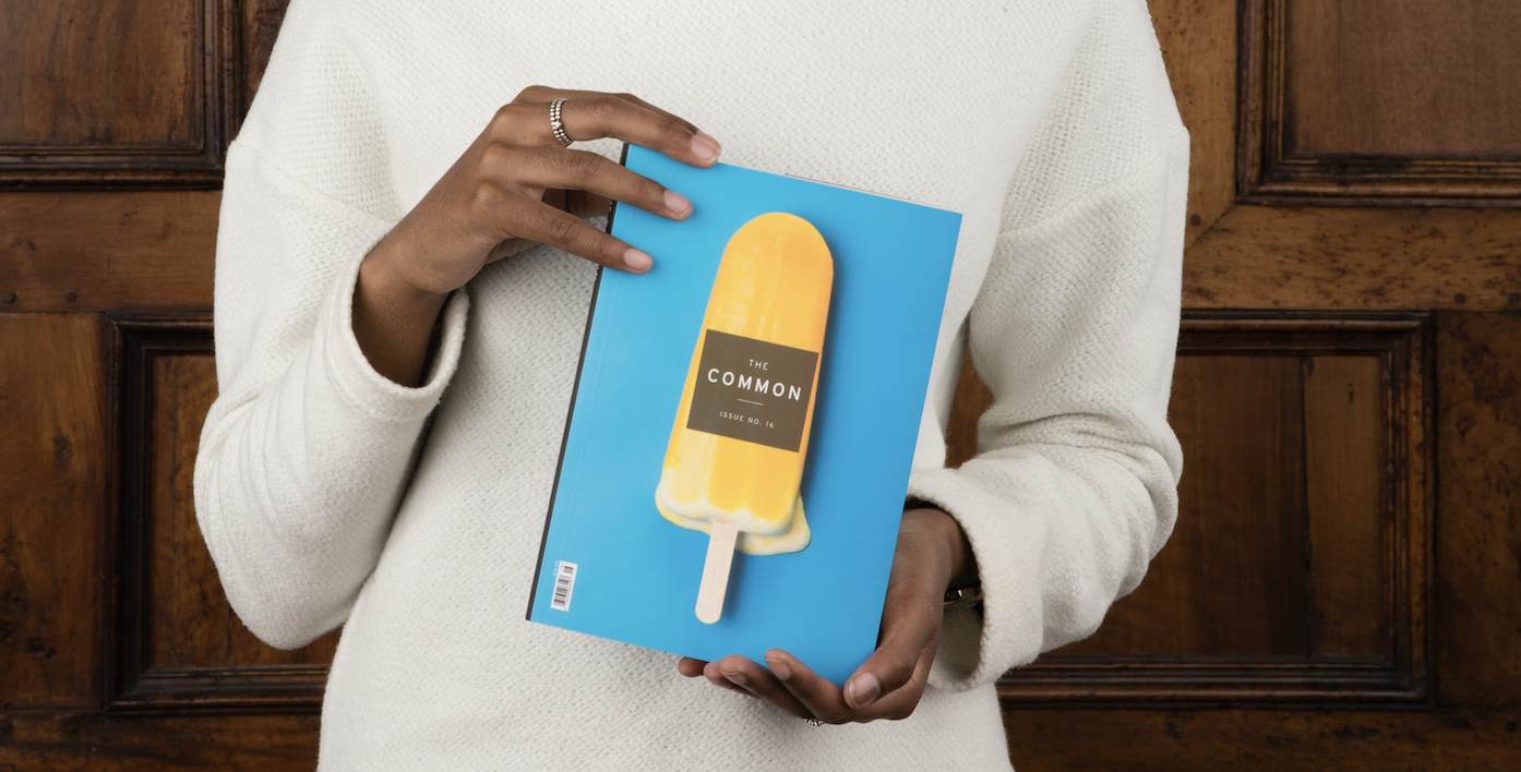 woman in a white sweater with dark skin holding Issue 16 of The Common (which is bright blue with a yellow popsicle)