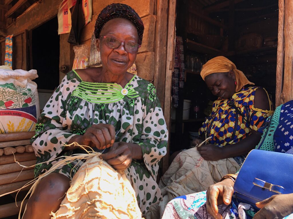 Two people sitting next to each other in front of a house, holding textiles.