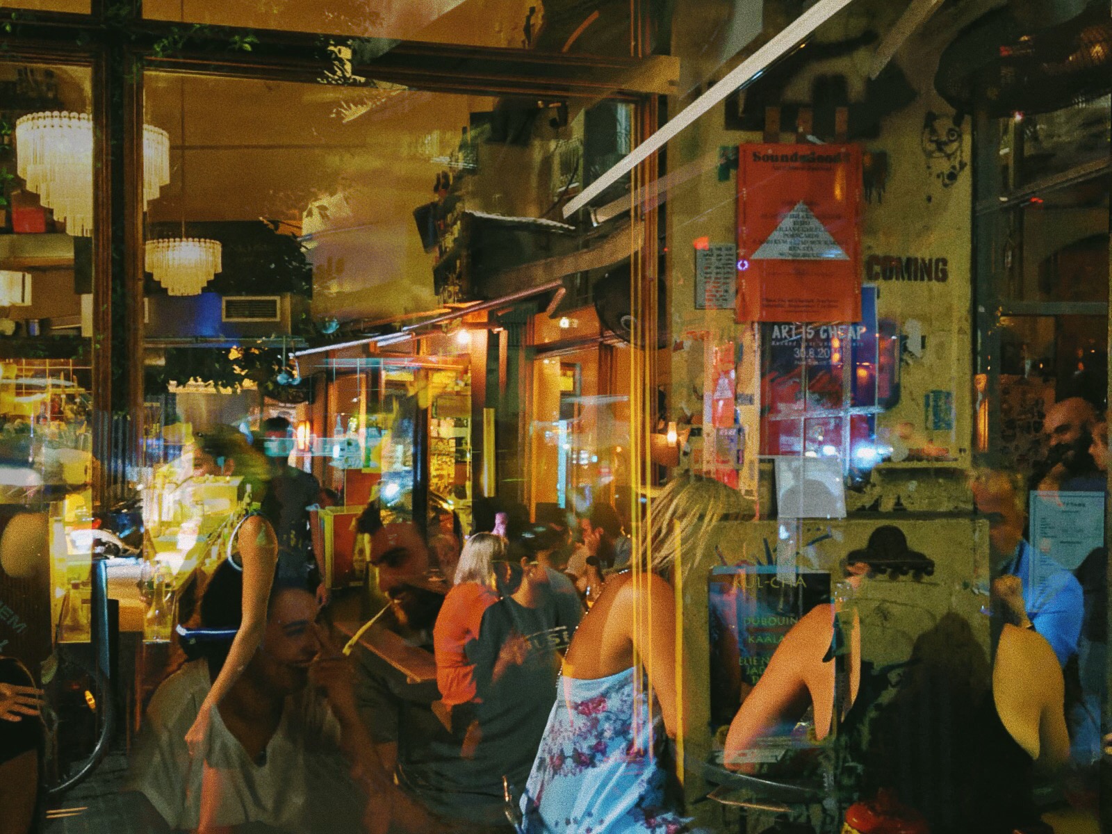 A photograph of people sitting in a restaurant through a glass window. The reflections of the people make the image blurry.