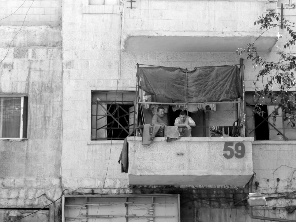Two people hang laundry from a balcony