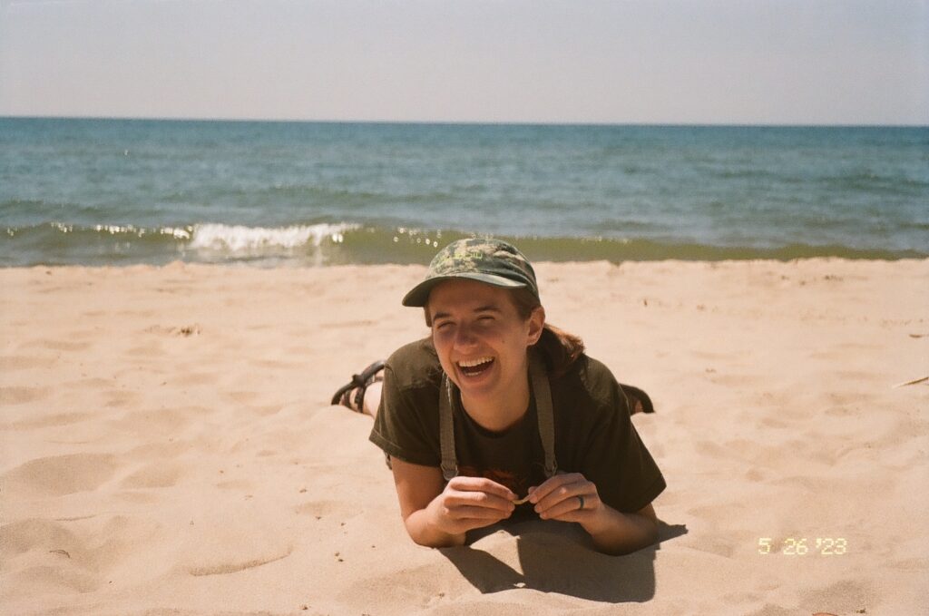 a smiling person lying on their stomach on a beach. the photo has a sepia-toned filter 