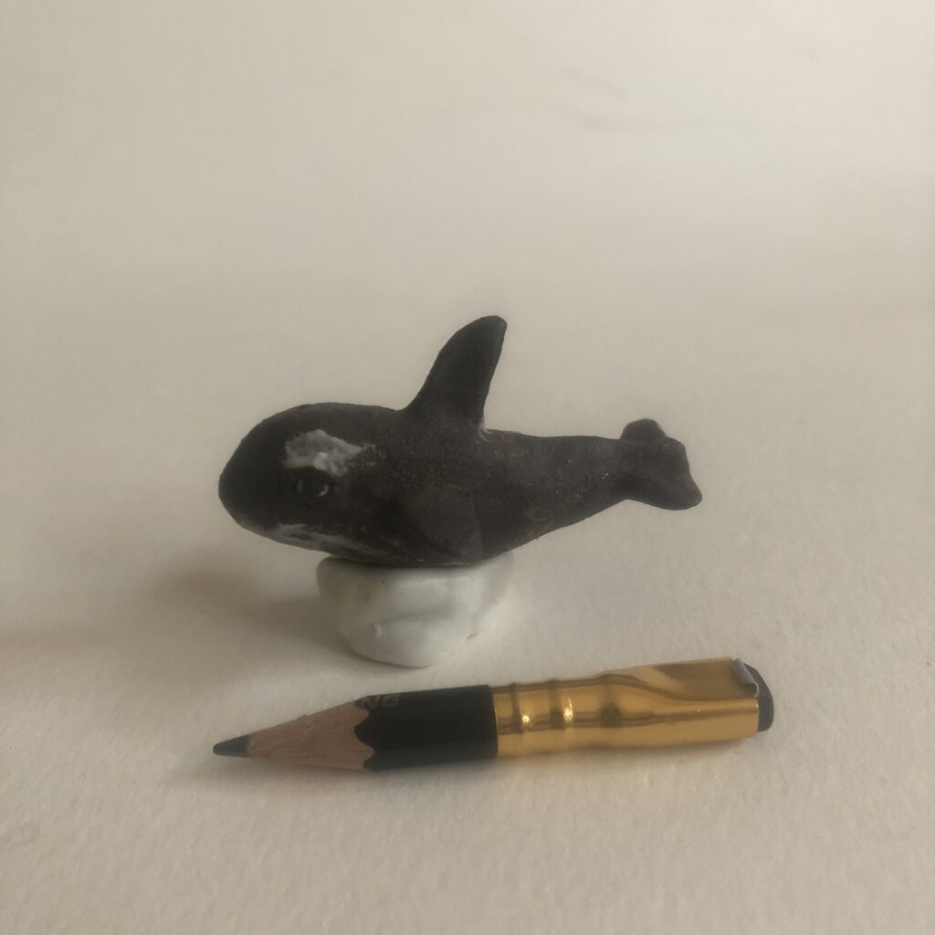 small whale sculpture on white background next to pencil