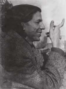 Portrait of person smiling and holding up their hand. Turned to the right.